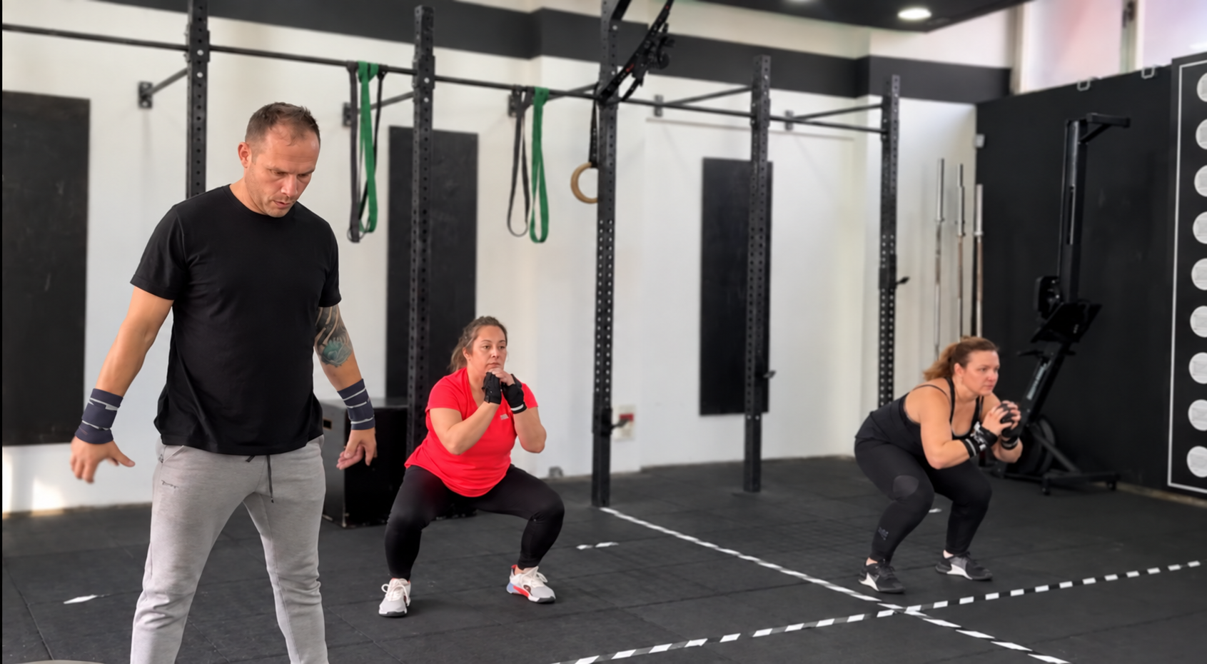 Entrenador y dos mujeres realizando variantes de sentadilla en una sesión de Estudio Training.